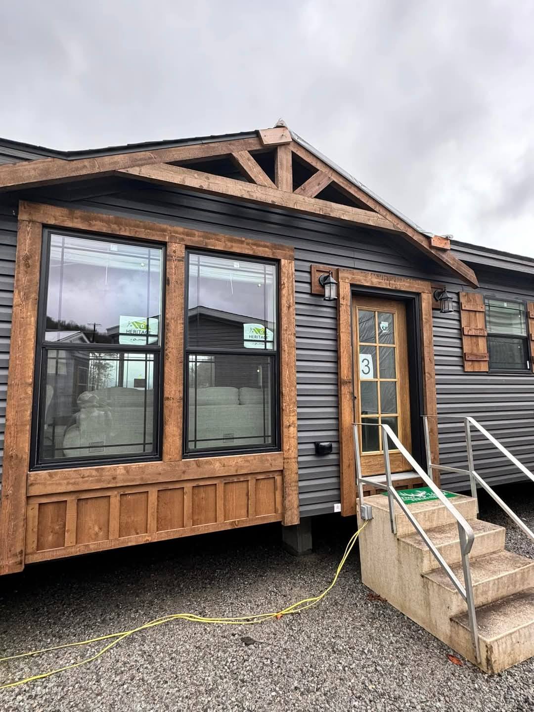 Cozy cabin with dark siding and wooden accents under a cloudy sky. Features large windows, a front door with the number 3, and stair access.