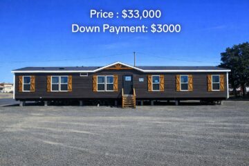 Single-story dark brown manufactured home with light brown shutters on a sunny day. Price $33,000, down payment $3,000. Stands on a gravel lot.