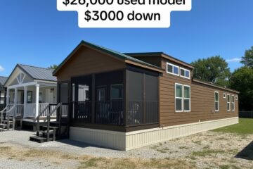 Small brown manufactured home with a screened porch sits in a lot beside other homes. Clear blue sky above. Text reads: "$26,000 used model, $3000 down."