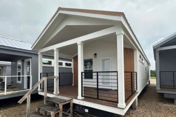Modern tiny home with white siding and a wooden front porch, featuring black railings and a gable roof. The atmosphere is cozy and inviting.