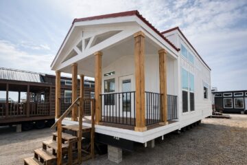 A modern tiny house with a red roof features a wood-trimmed porch and multiple glass windows, conveying a cozy and minimalist aesthetic.