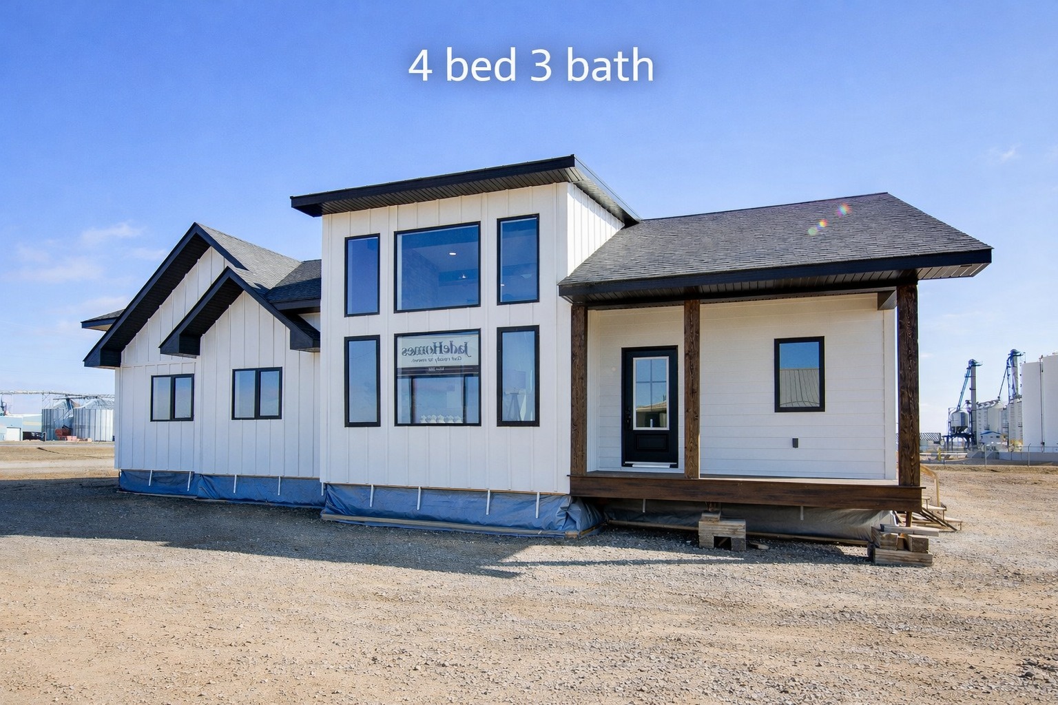 Modern white modular home with dark trim, featuring large windows, a small porch, and a gabled roof. Text reads "4 bed 3 bath" against a clear blue sky.