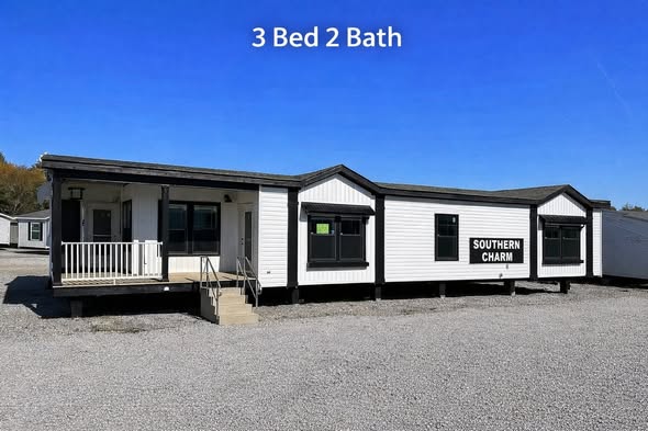 A white mobile home labeled "Southern Charm" with a small porch and steps is set against a clear blue sky. Text reads “3 Bed 2 Bath.” Gravel surrounds the home.