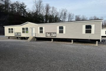 A beige mobile home on display in a gravel lot, featuring a "5 Bed 3 Bath" sign, priced at $35,900. Bare trees and overcast sky in the background.