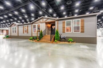A modern manufactured home is showcased indoors with wood accents and lush plants around the entrance, creating a welcoming and stylish appearance.