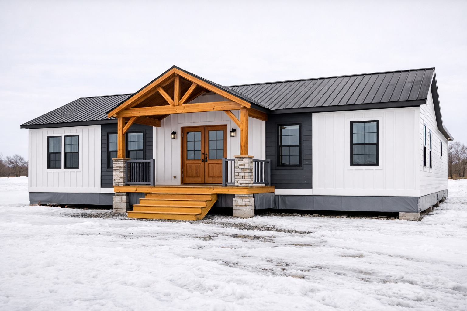 A modern prefab home in a snowy landscape. It features a black metal roof, white and gray siding, and a wooden porch with stone accents, exuding a cozy, inviting feel.