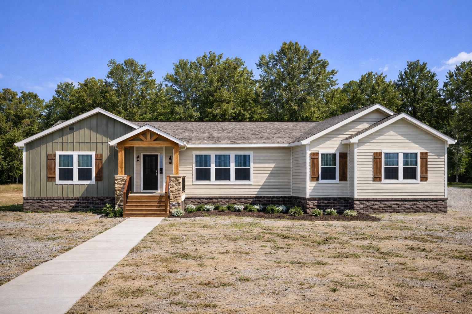 Single-story beige and green modular home with a gabled roof, wooden porch, and stone accents. Set against lush trees under a clear blue sky.