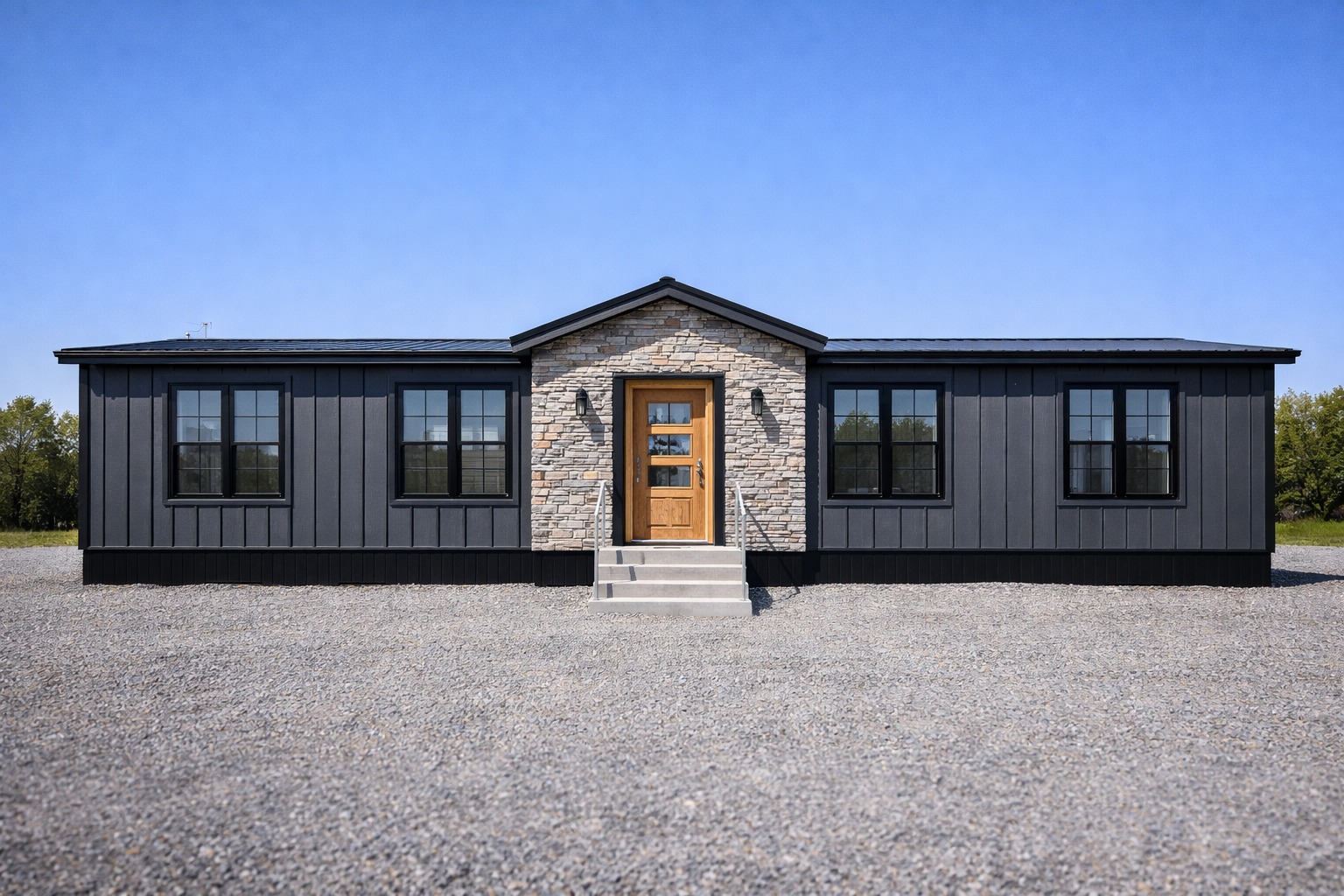 Single-story modern house under blue sky features dark siding, a stone-accented entryway with a wooden door, and symmetrical windows, creating a welcoming, balanced look.