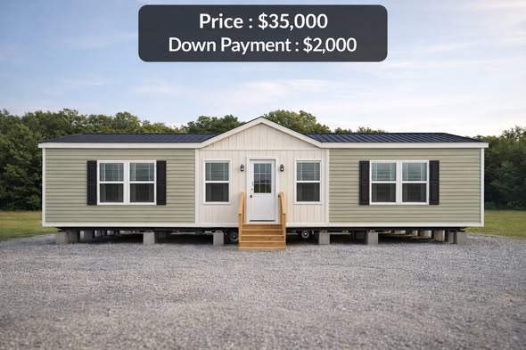 A beige and white mobile home with black shutters sits on a gravel lot, surrounded by trees under a clear sky. Price: $35,000, Down Payment: $2,000.
