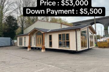 Mobile home for sale in a yard, priced at $53,000 with a $5,500 down payment. Surrounded by trees and industrial structures, overcast sky.
