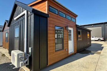 Modern tiny house with wood and black paneling under a clear blue sky. Price: $35,000. Down payment: $8,000. Air conditioning unit attached.