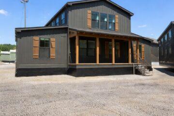 A modern dark gray two-story building with wooden shutters and porch under a clear blue sky. Gravel parking area in the foreground, creating a peaceful scene.