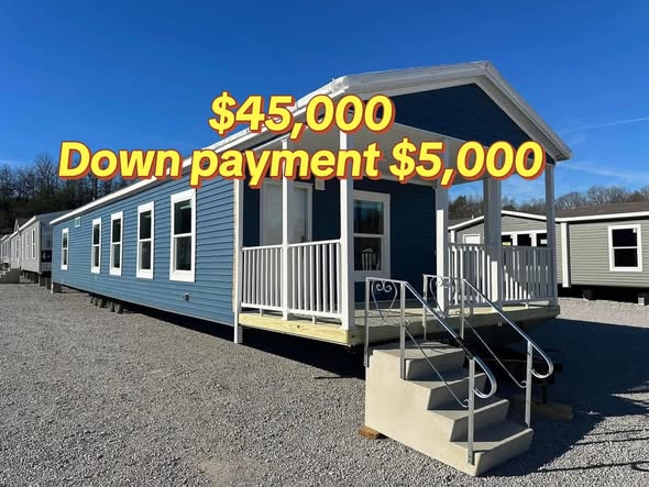 A blue manufactured home with a small covered porch and metal stairs, set on gravel. Text overlay indicates "$45,000" and "Down payment $5,000."