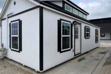 Small white house with black-trimmed windows and a white front door on a concrete slab. Overcast sky sets a neutral tone. Modern and compact.