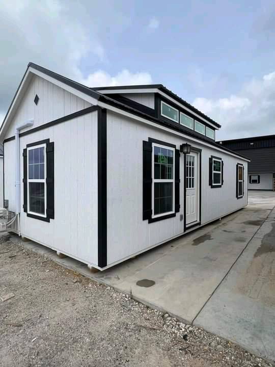 Small white house with black-trimmed windows and a white front door on a concrete slab. Overcast sky sets a neutral tone. Modern and compact.