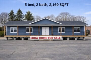 Blue modular home with a white door, railing, and a porch on a large lot. Text above reads "5 bed, 2 bath, 2,160 SQFT." Sign says "Show Home For Sale."