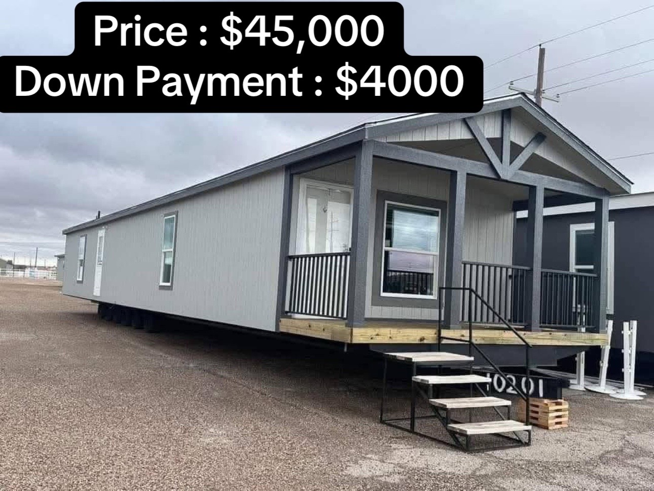A gray modular home with a small front porch and stairs, set on a gravel lot. Text above shows price $45,000, down payment $4,000. Overcast sky.